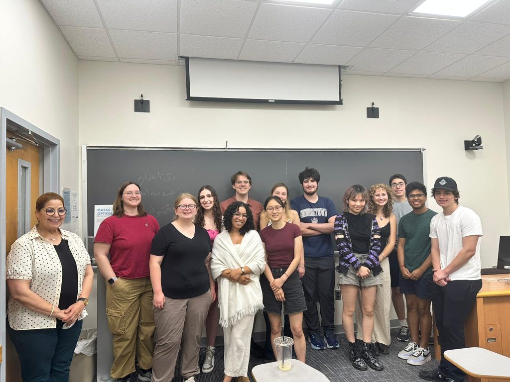 Ali is second from the left in a group of students that are standing in front of a blackboard in a classroom.